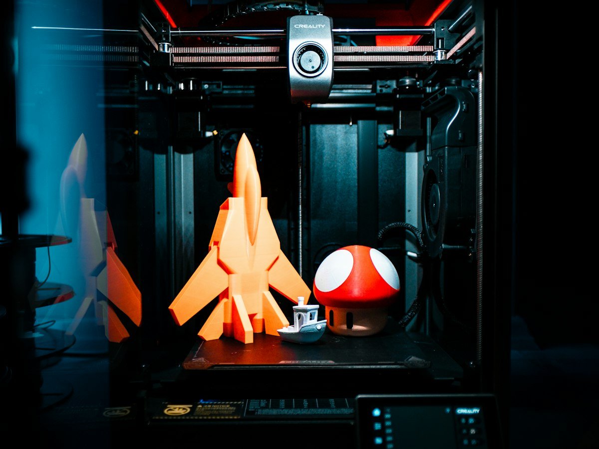 3D printer with freshly printed orange parts on the build plate